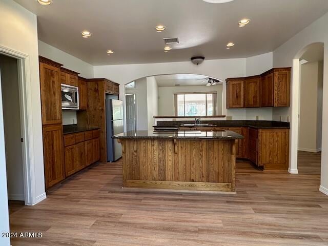 kitchen with dark stone countertops, appliances with stainless steel finishes, wood-type flooring, sink, and a center island