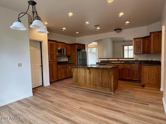 kitchen featuring stainless steel microwave, fridge, hanging light fixtures, light hardwood / wood-style flooring, and a kitchen island