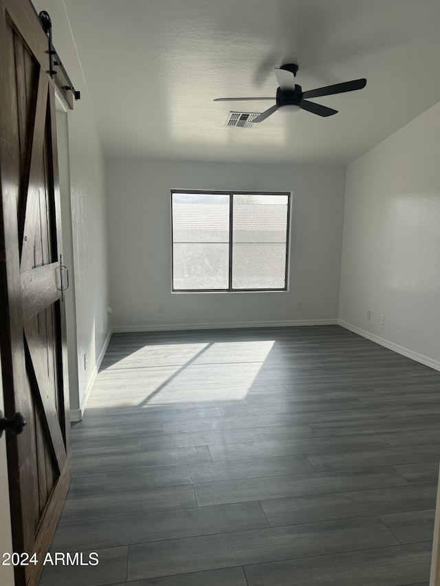 spare room with a barn door, dark hardwood / wood-style floors, and ceiling fan