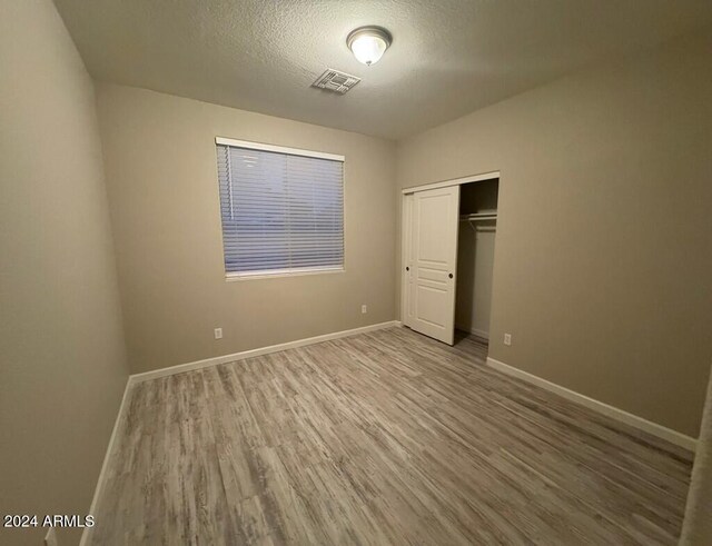 unfurnished bedroom with light hardwood / wood-style floors, a textured ceiling, and a closet