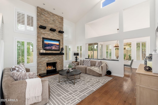 living room featuring wood-type flooring, high vaulted ceiling, baseboards, and a stone fireplace