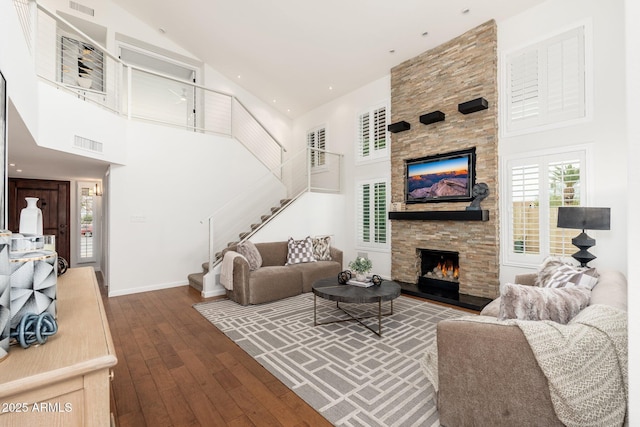 living area with a stone fireplace, a high ceiling, visible vents, stairs, and wood-type flooring