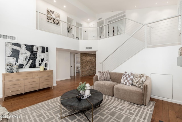 living room with hardwood / wood-style floors, a towering ceiling, and visible vents