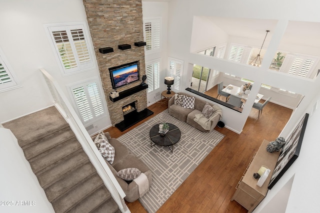 living room featuring a towering ceiling, hardwood / wood-style flooring, stairs, and a stone fireplace