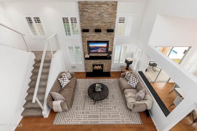 living area with baseboards, stairway, wood finished floors, a high ceiling, and a stone fireplace