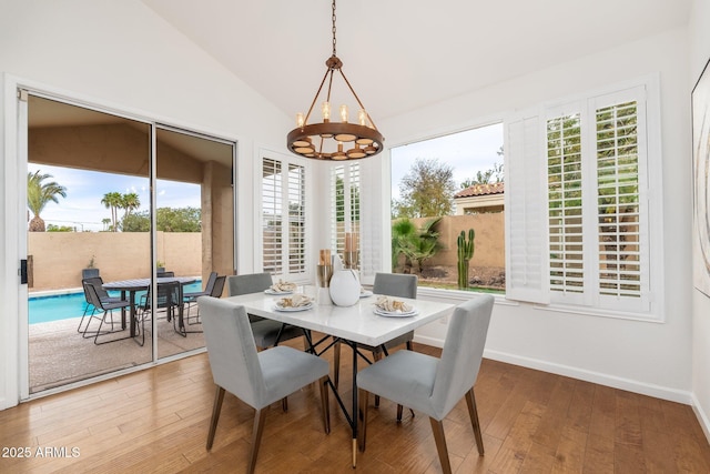 dining space featuring light wood-style floors, lofted ceiling, a chandelier, and baseboards