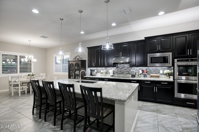 kitchen featuring pendant lighting, a center island with sink, appliances with stainless steel finishes, a kitchen breakfast bar, and sink