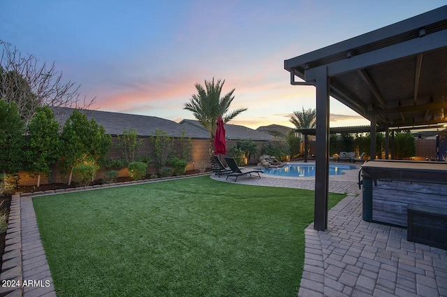 yard at dusk featuring a swimming pool with hot tub and a patio area