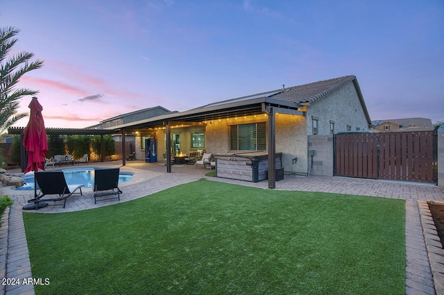 back house at dusk featuring a yard and a patio