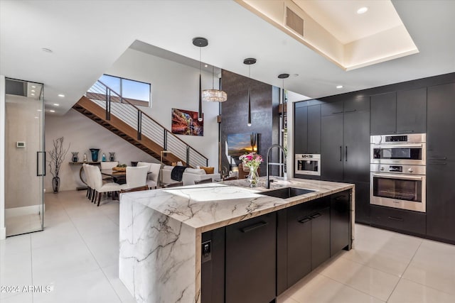 kitchen with sink, hanging light fixtures, double oven, a kitchen island with sink, and light tile patterned floors