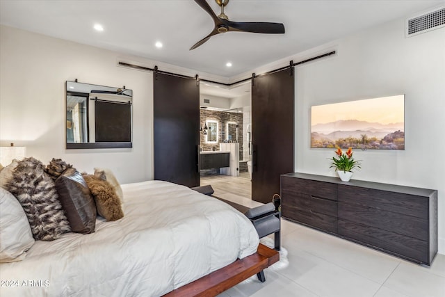 tiled bedroom featuring a barn door, ceiling fan, and connected bathroom