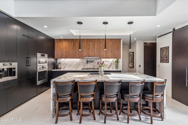 kitchen with backsplash, a barn door, a spacious island, and decorative light fixtures