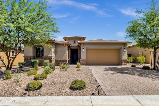 prairie-style home featuring an attached garage, stone siding, decorative driveway, and stucco siding