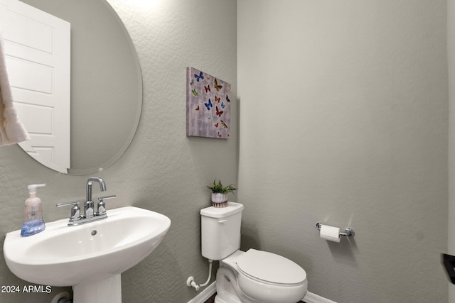 half bath featuring a textured wall, baseboards, a sink, and toilet