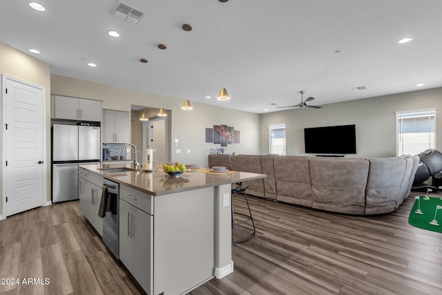 kitchen with pendant lighting, stainless steel appliances, open floor plan, a kitchen island with sink, and a sink