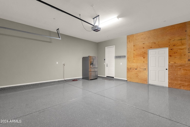 garage featuring wood walls, a garage door opener, and stainless steel fridge with ice dispenser