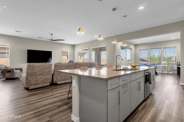 kitchen with light countertops, hanging light fixtures, open floor plan, a sink, and an island with sink