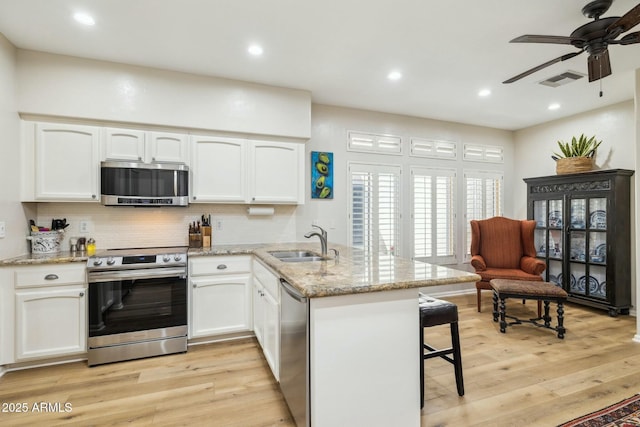 kitchen with a sink, white cabinets, a peninsula, and stainless steel appliances