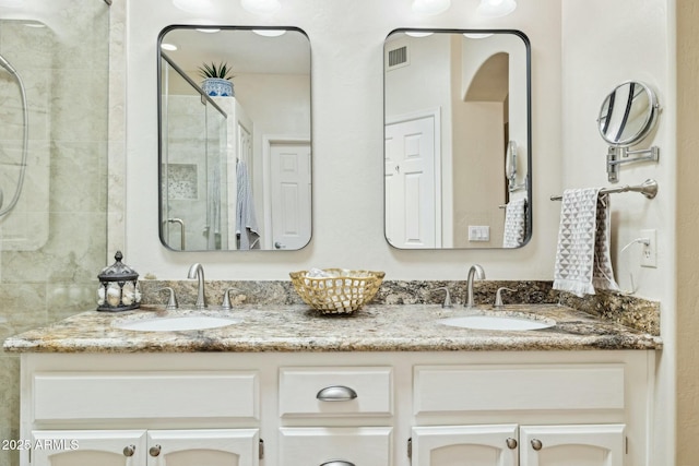 bathroom featuring double vanity, visible vents, a tile shower, and a sink