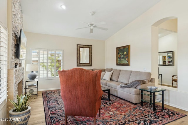living area with lofted ceiling, arched walkways, light wood finished floors, a ceiling fan, and a fireplace