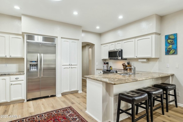 kitchen with stainless steel appliances, arched walkways, light stone counters, white cabinets, and a peninsula