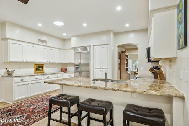 kitchen featuring visible vents, a peninsula, appliances with stainless steel finishes, a sink, and light stone counters