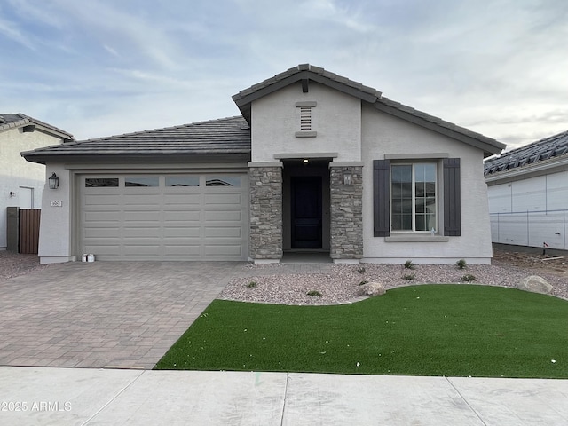 view of front of home with decorative driveway, a tile roof, stucco siding, a garage, and stone siding