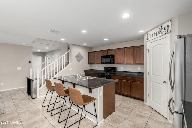 kitchen featuring sink, an island with sink, a breakfast bar, light tile patterned floors, and black appliances