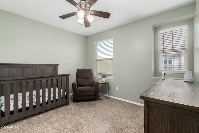 carpeted bedroom with a crib and ceiling fan