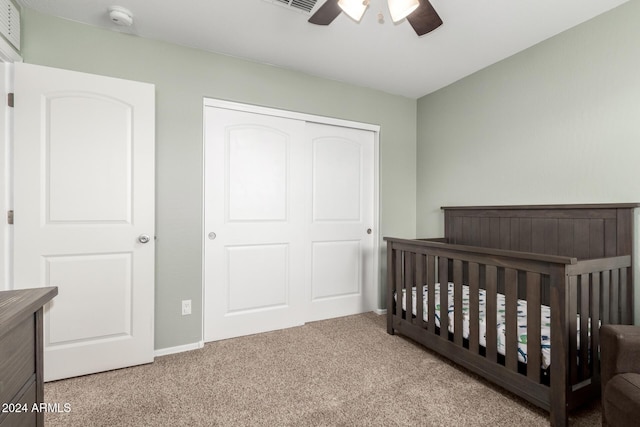 bedroom with ceiling fan, a closet, light carpet, and a crib