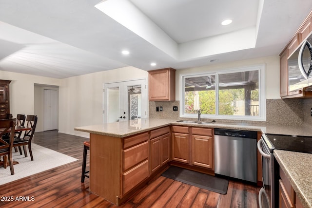 kitchen with dark wood finished floors, a peninsula, stainless steel appliances, and a sink