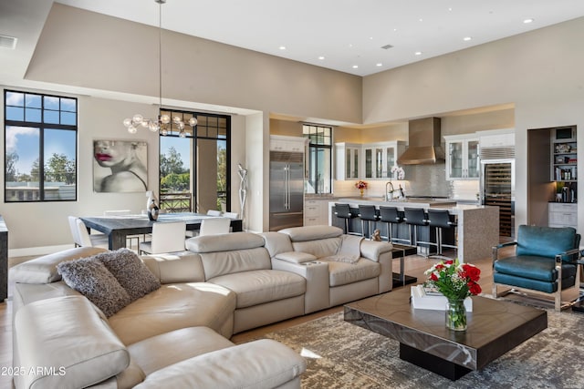 living area featuring a chandelier, a towering ceiling, recessed lighting, beverage cooler, and baseboards