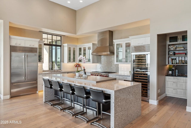 kitchen featuring stainless steel appliances, wall chimney range hood, beverage cooler, a center island, and white cabinetry