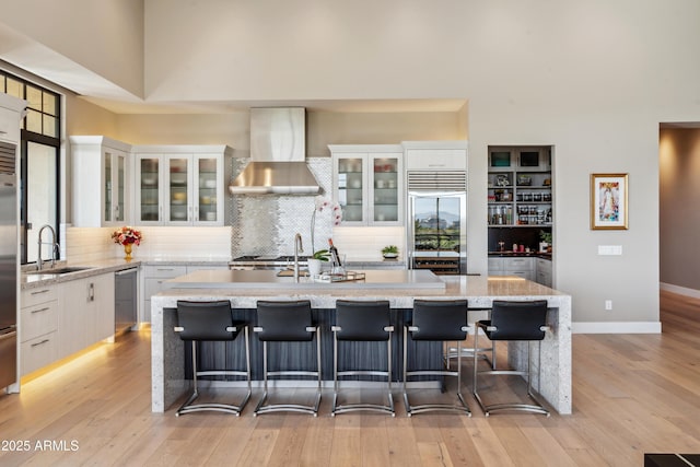 kitchen with wall chimney range hood, a sink, appliances with stainless steel finishes, a kitchen island with sink, and decorative backsplash