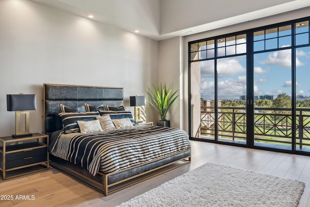 bedroom with access to exterior, wood finished floors, recessed lighting, and a towering ceiling