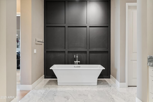 full bath featuring marble tiled floors, a soaking tub, and baseboards