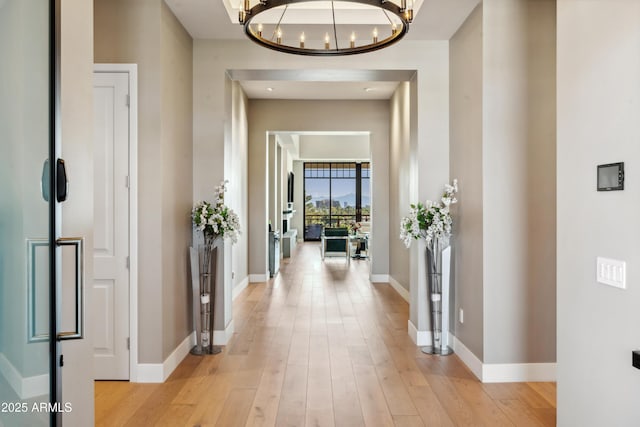 hall featuring a chandelier, light wood-type flooring, and baseboards