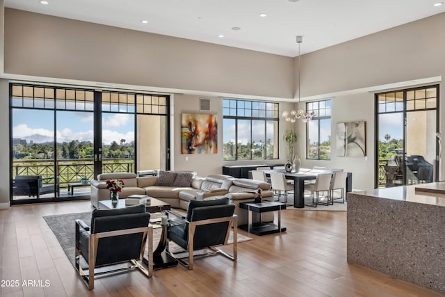 living area featuring hardwood / wood-style floors, healthy amount of natural light, a high ceiling, recessed lighting, and a chandelier