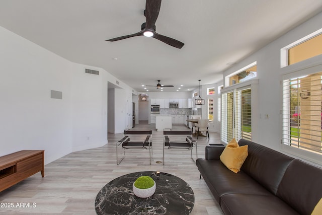 living area featuring baseboards, light wood-type flooring, visible vents, and a ceiling fan