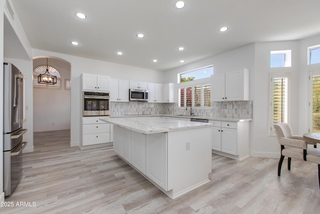 kitchen featuring a sink, white cabinets, appliances with stainless steel finishes, a center island, and tasteful backsplash