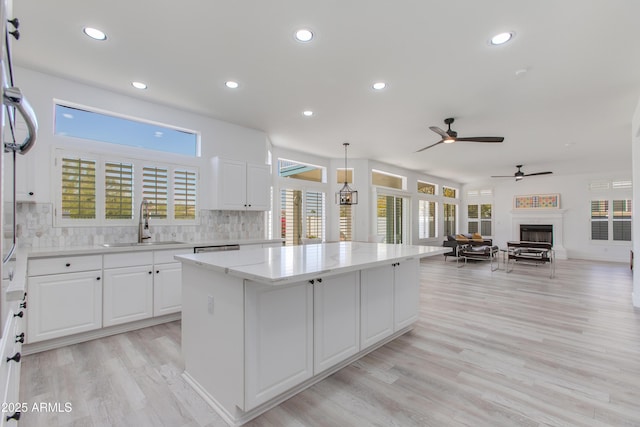 kitchen with a center island, a fireplace, open floor plan, white cabinetry, and a sink