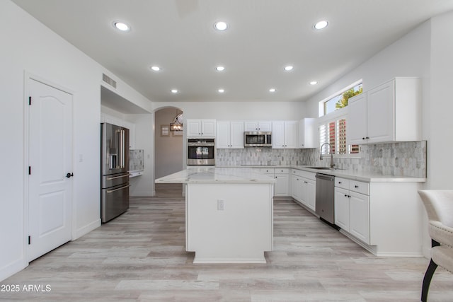 kitchen featuring arched walkways, stainless steel appliances, a kitchen island, a sink, and white cabinets