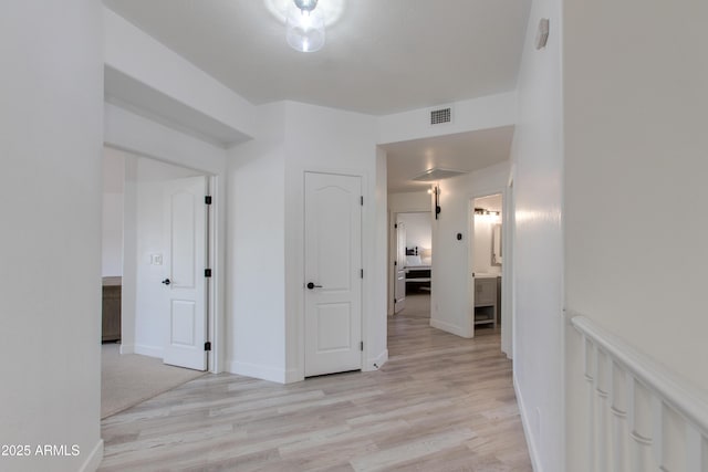 hall with light wood-style floors, baseboards, and visible vents