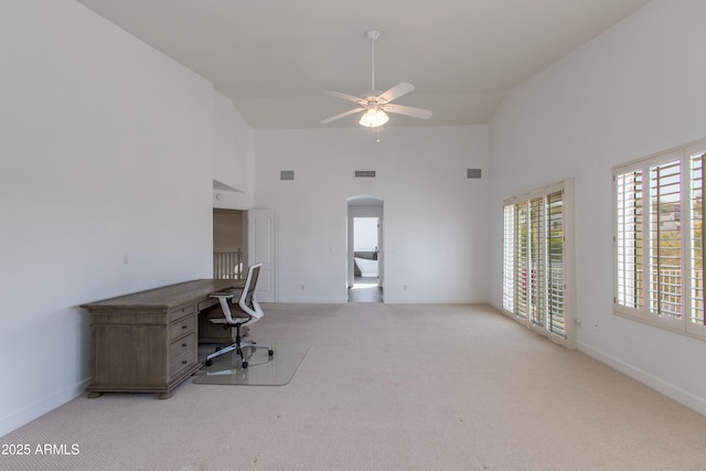 unfurnished office with carpet floors, arched walkways, ceiling fan, and a towering ceiling