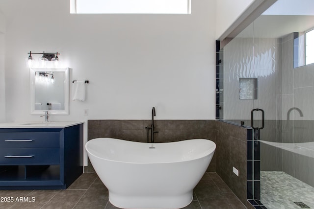 bathroom with tile walls, a freestanding bath, a stall shower, vanity, and tile patterned flooring