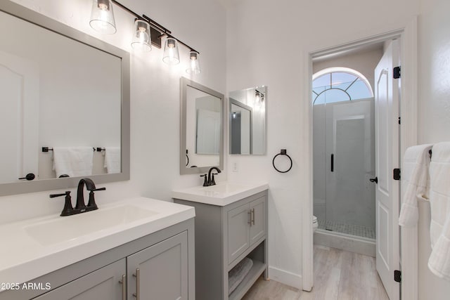 full bath featuring wood finished floors, a stall shower, two vanities, and a sink