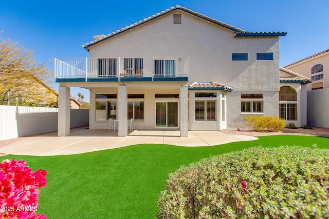 rear view of house featuring stucco siding, a lawn, a patio area, fence, and a balcony