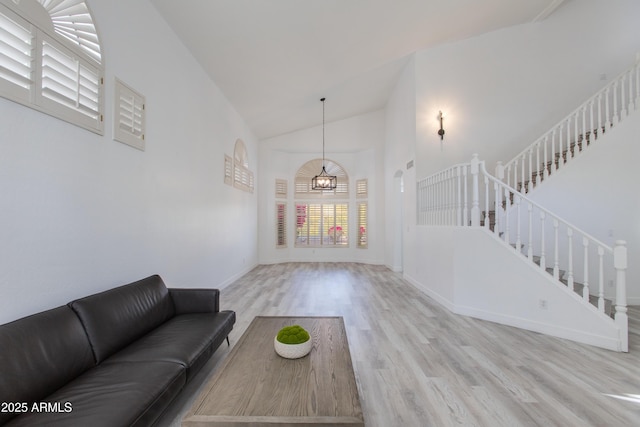 living room featuring high vaulted ceiling, wood finished floors, baseboards, stairs, and an inviting chandelier