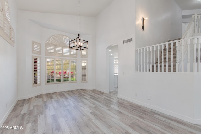 unfurnished room featuring arched walkways, visible vents, a towering ceiling, wood finished floors, and baseboards