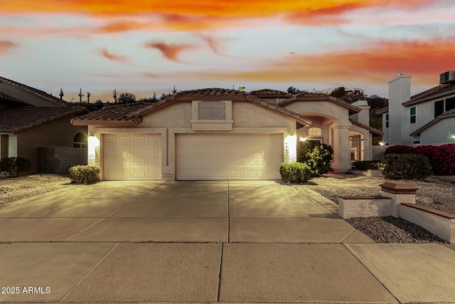 mediterranean / spanish house with an attached garage, a tiled roof, concrete driveway, and stucco siding